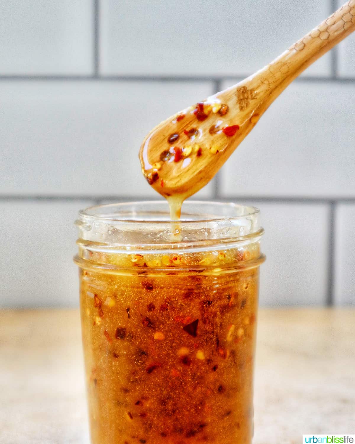 honey spoon lifting hot honey sauce out of a mason jar with subway tile kitchen backsplash.