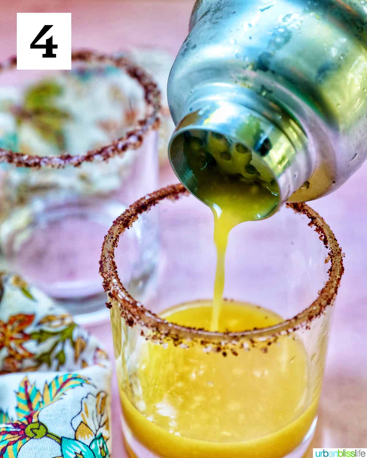 cocktail shaker pouring spicy mango margarita into a glass.