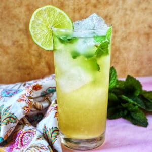 glass of Mango mojito with mint leaves, ice cubes, and a lime slice garnish.