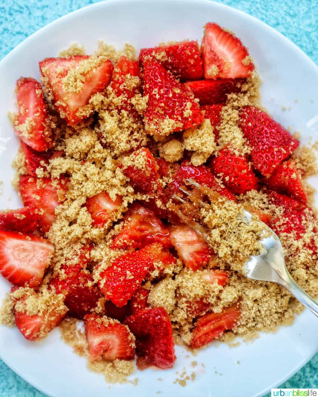 a fork mashing fresh strawberries and brown sugar together.