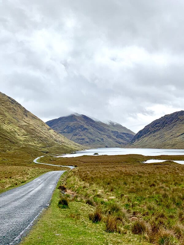 narrow road in ireland with large hills in background