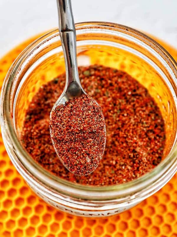 hand holding a spoon in a jar of homemade taco seasoning on a yellow mat.