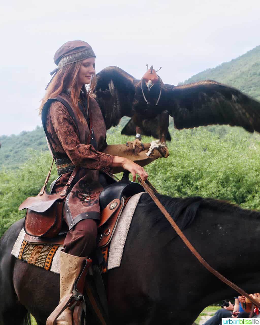 falcon trainer holding a large falcon on her arm while riding horseback at Falcon Farm in Almaty Kazakhstan.