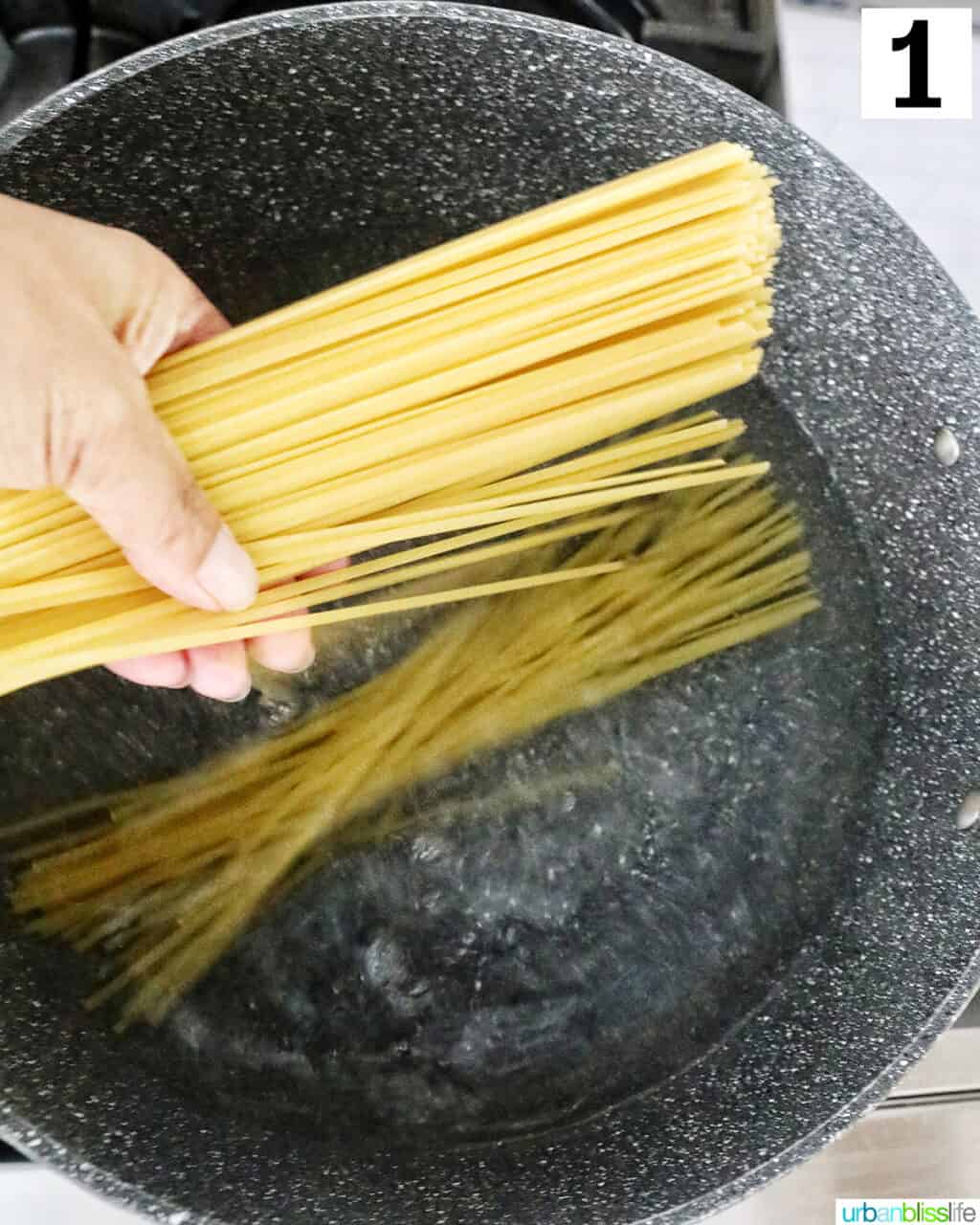 hand lowering linguine pasta into a large pot of water.