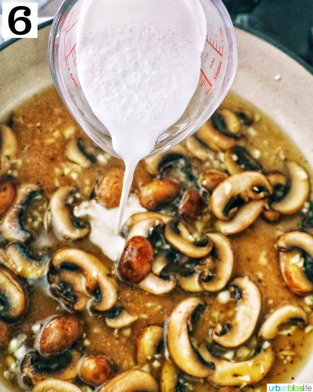 pouring cream over chopped mushrooms cooking in a pan.