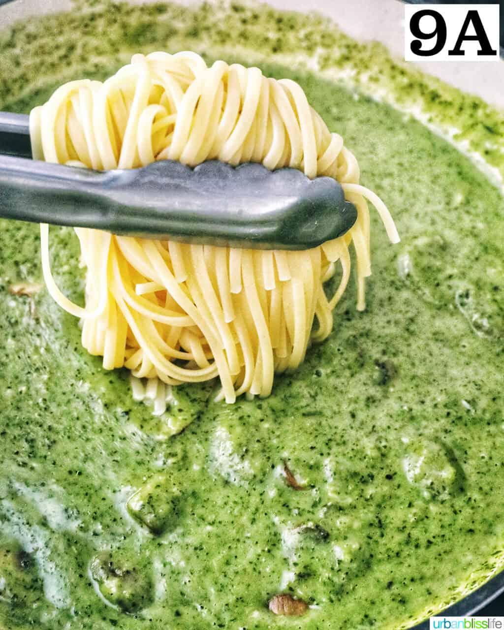 kitchen tongs lowering linguine pasta into pesto sauce with chopped mushrooms.