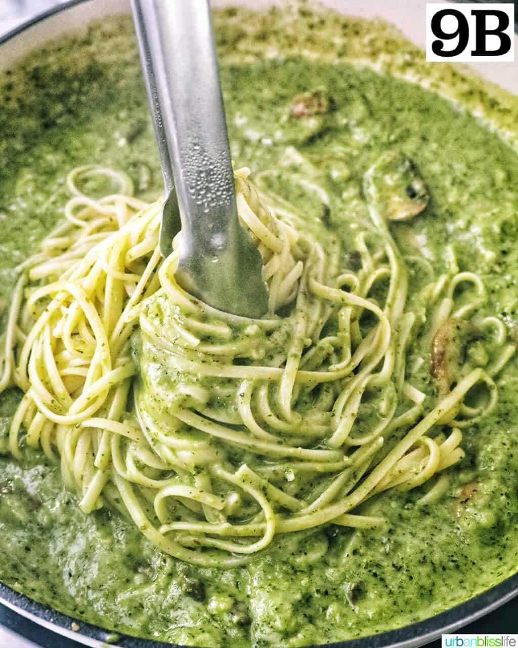 kitchen tongs twirling linguine pasta in pesto sauce with chopped mushrooms.