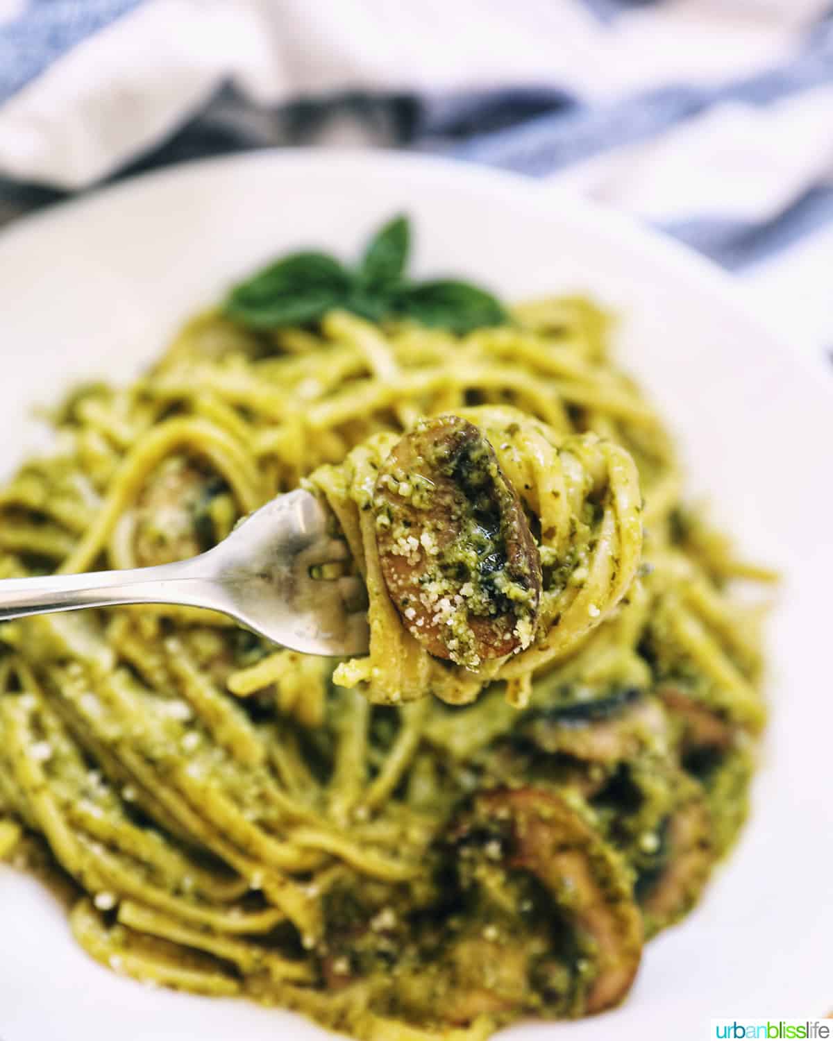fork twirling linguine pasta in pesto sauce with chopped mushrooms.
