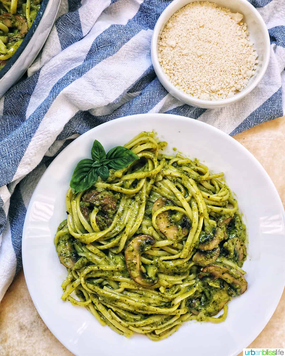 bowl of mushroom pesto pasta with a side of grated parmesan cheese.
