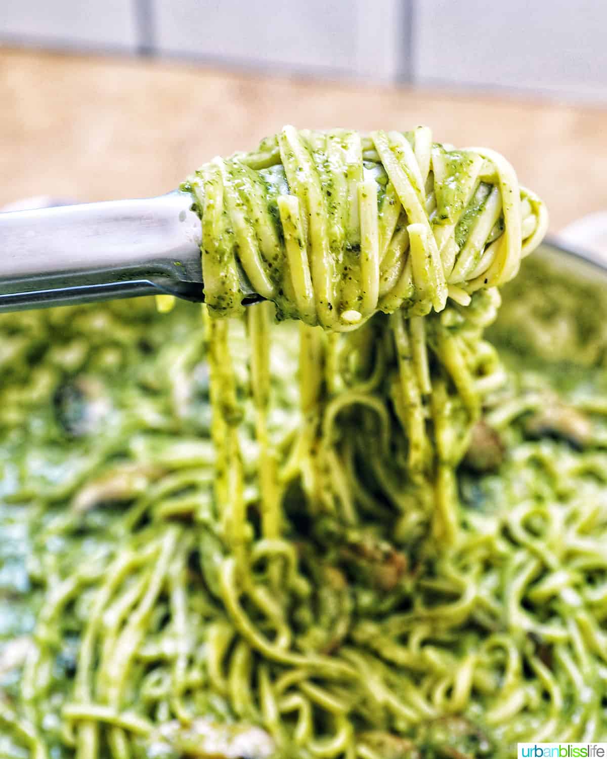 kitchen tongs twirling linguine pasta in pesto sauce with chopped mushrooms.