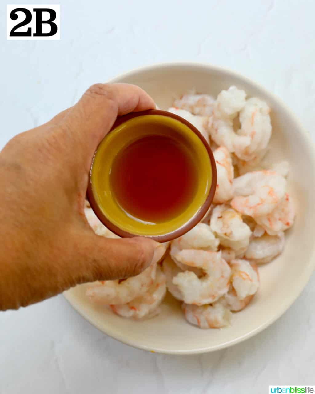 hand holding bowl of paprika over a bowl of prawns.