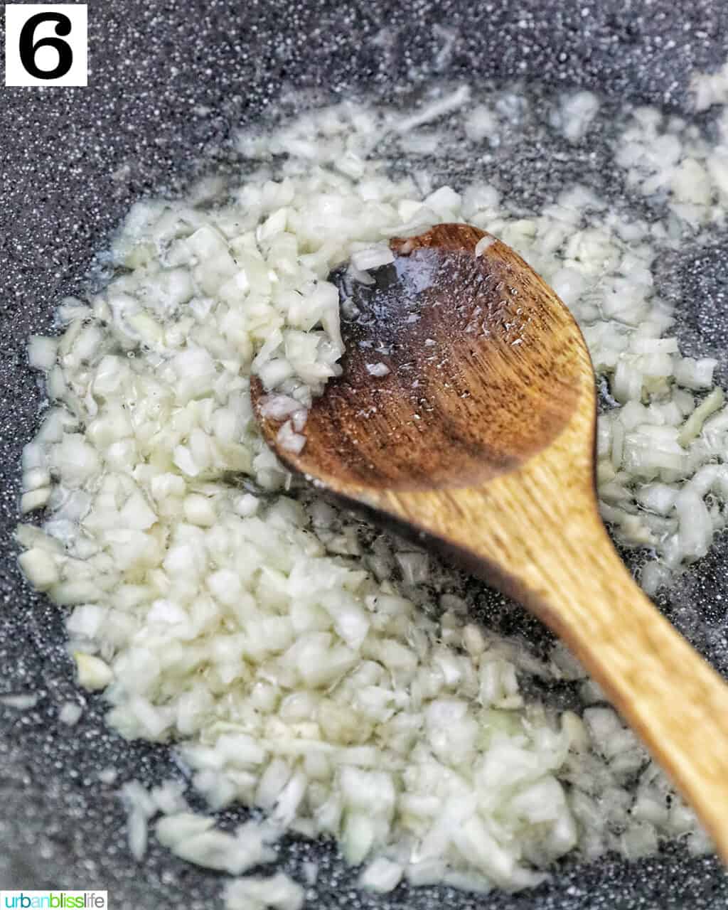 wooden spoon in a wok with garlic and onions.