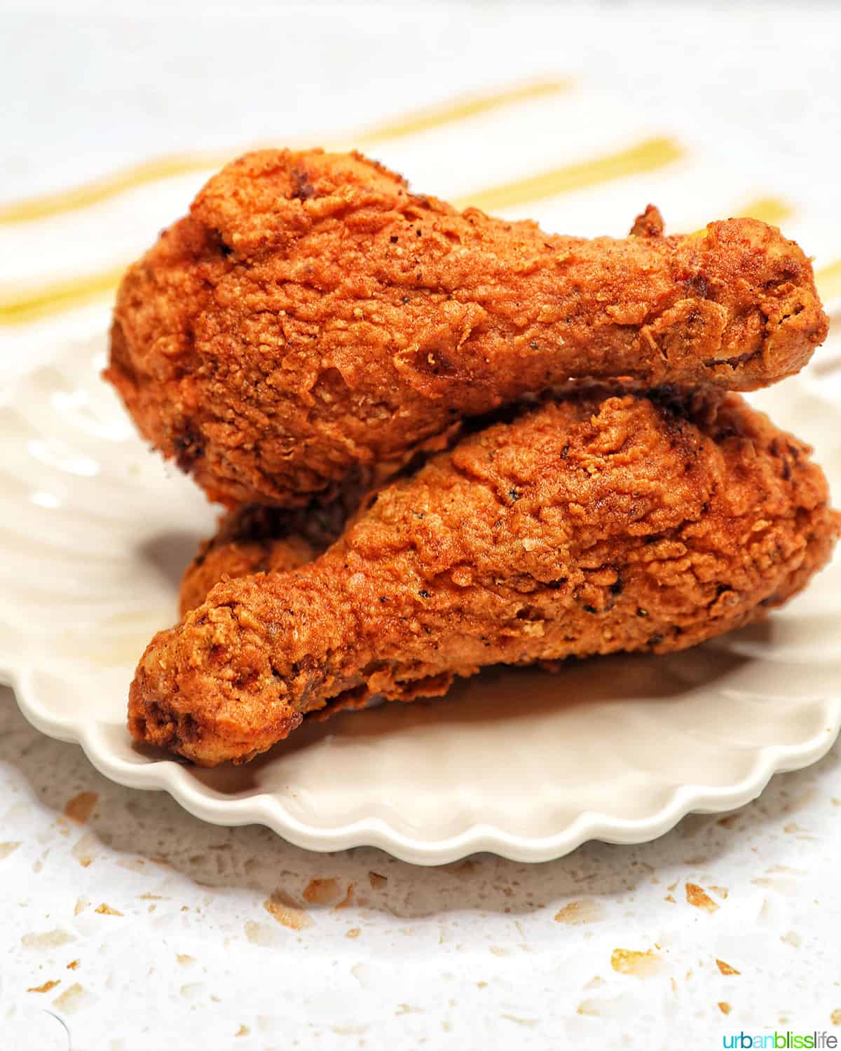 two fried chicken drumsticks stacked on a scalloped plate.