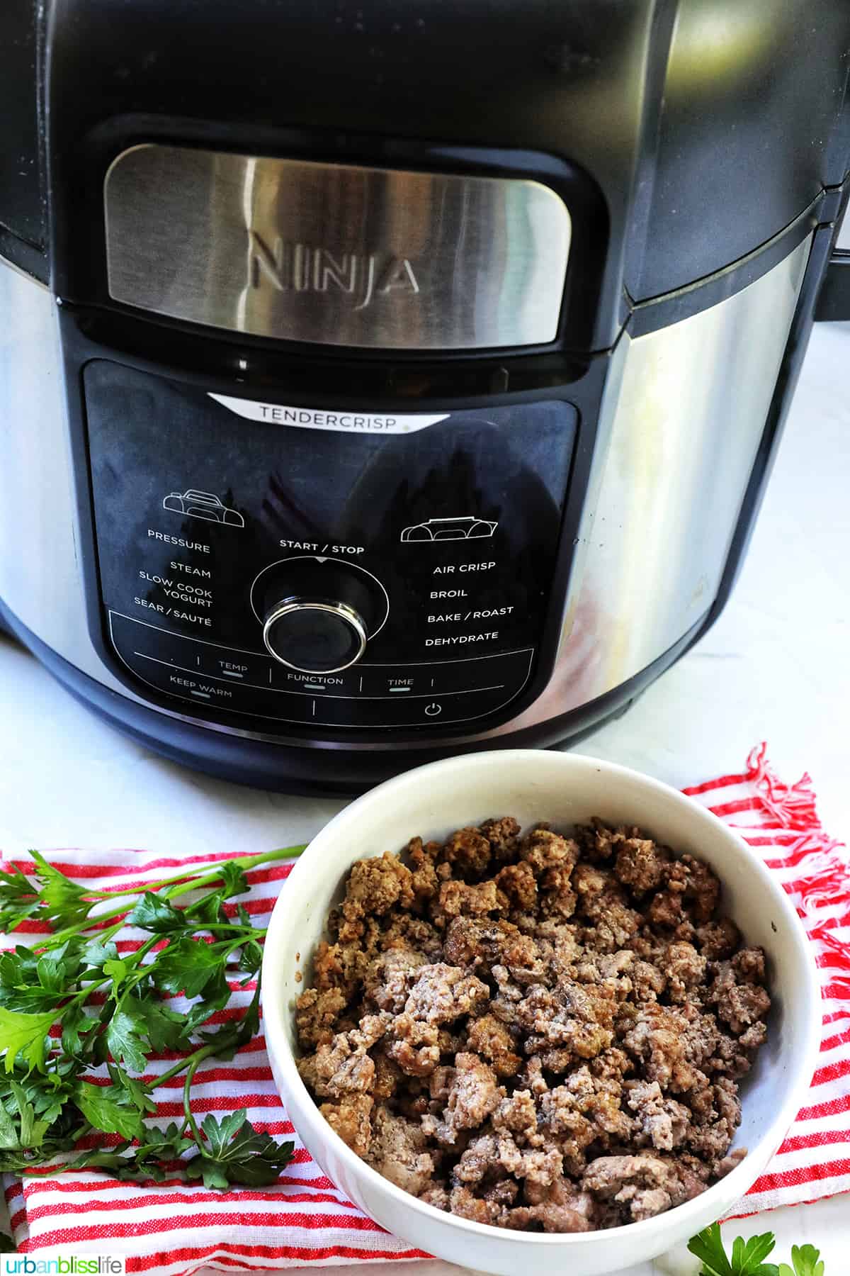 air fryer and ground beef in a white bowl with parsley sprigs around it and a red and white striped towel.