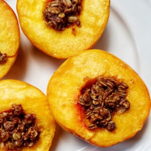 halved peaches with cinnamon oats topping on a white plate.