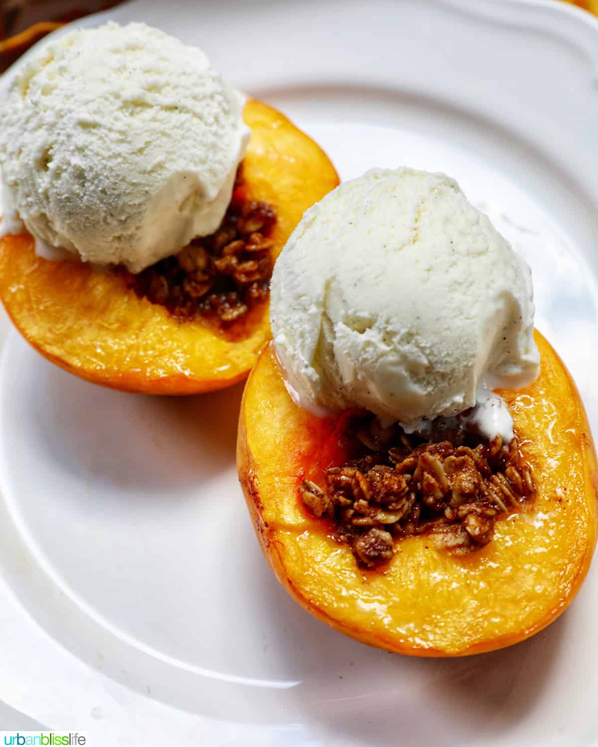 halved peaches with cinnamon oats topping with scoops of vanilla ice cream on a white plate.