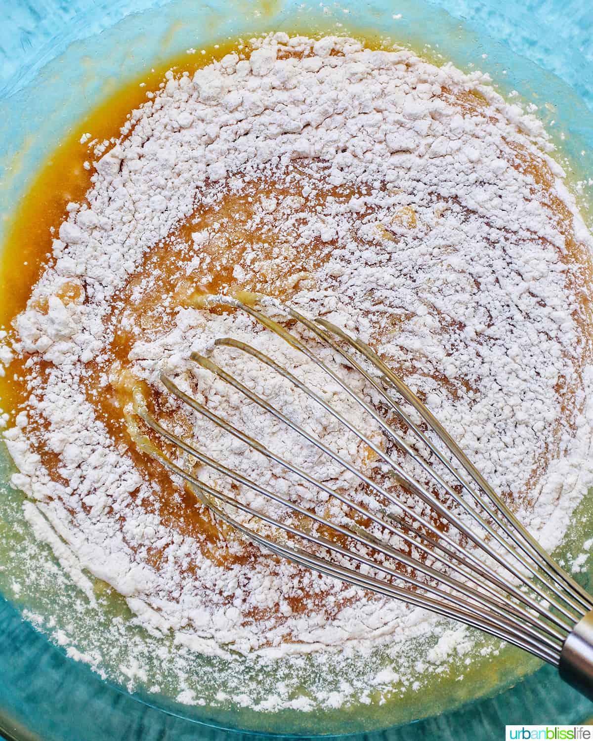 whisking dry ingredients into wet ingredients in a clear mixing bowl.