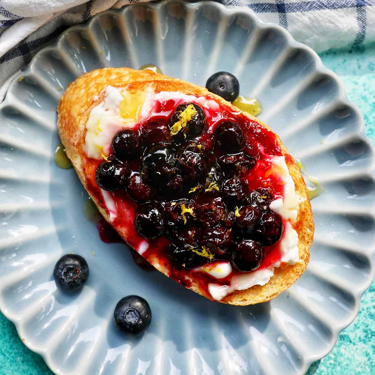 blueberries and cream cheese on toast on a blue scalloped plate.