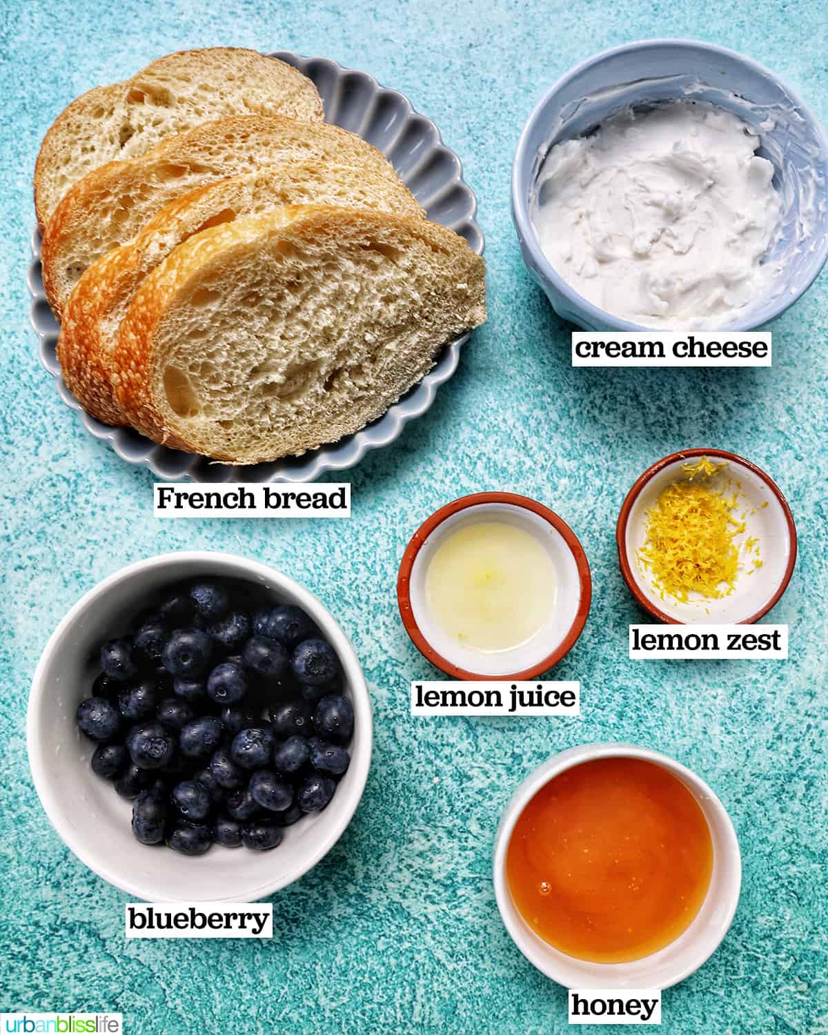 ingredients to make blueberry toast on separate plates and bowls on a blue table.