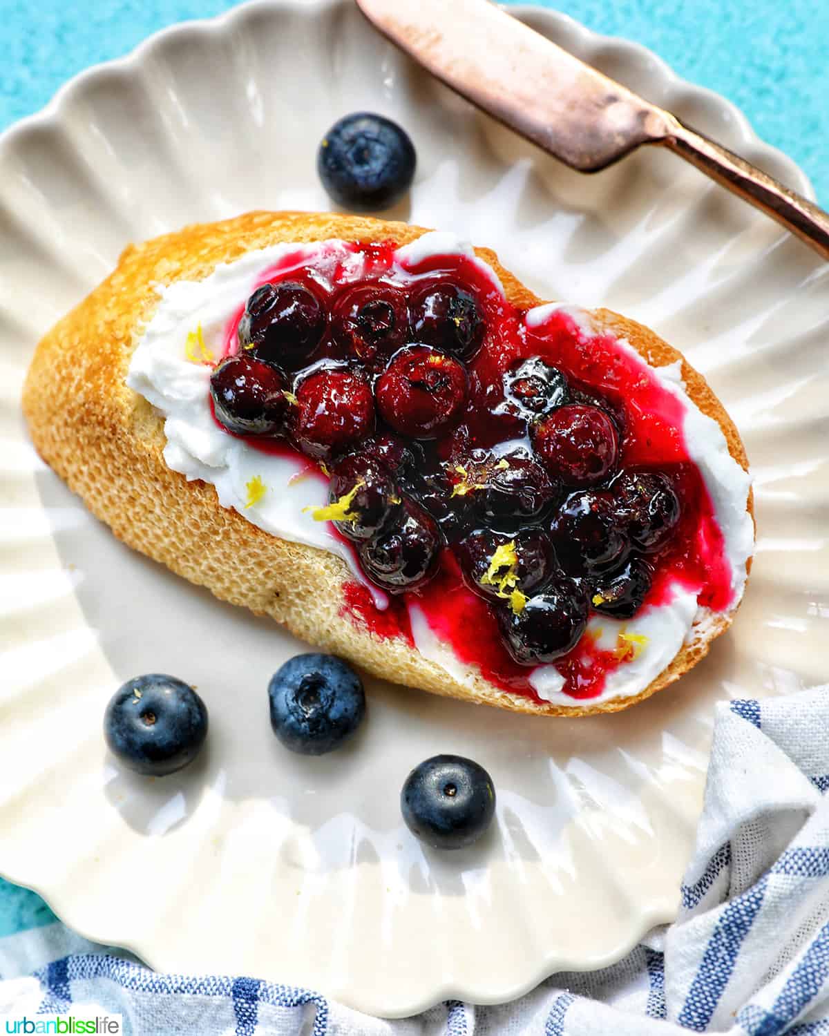 blueberries and cream cheese on toast on a white scalloped plate.