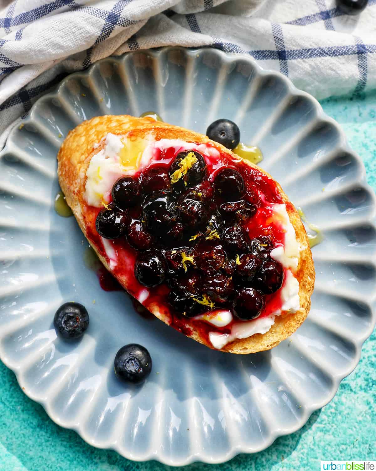 blueberries and cream cheese on toast on a blue scalloped plate.