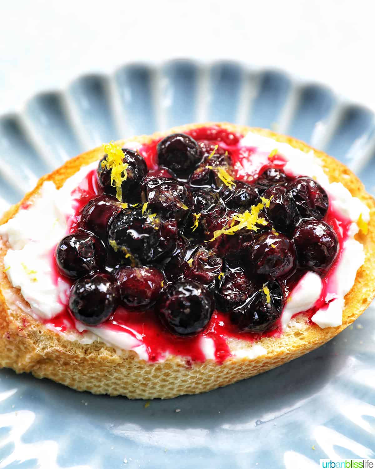 blueberries and cream cheese on toast on a blue scalloped plate.