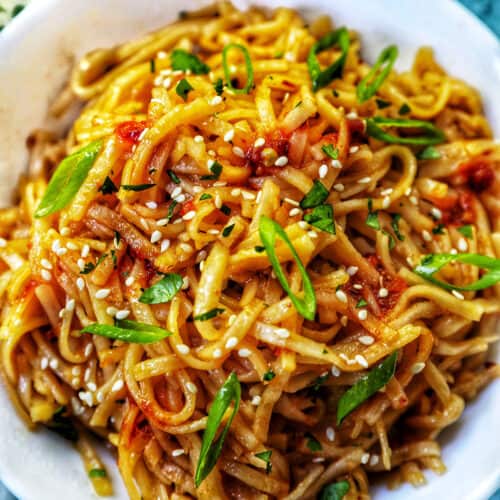 Chili Garlic Noodles with green onions and sesame seeds in a white bowl.