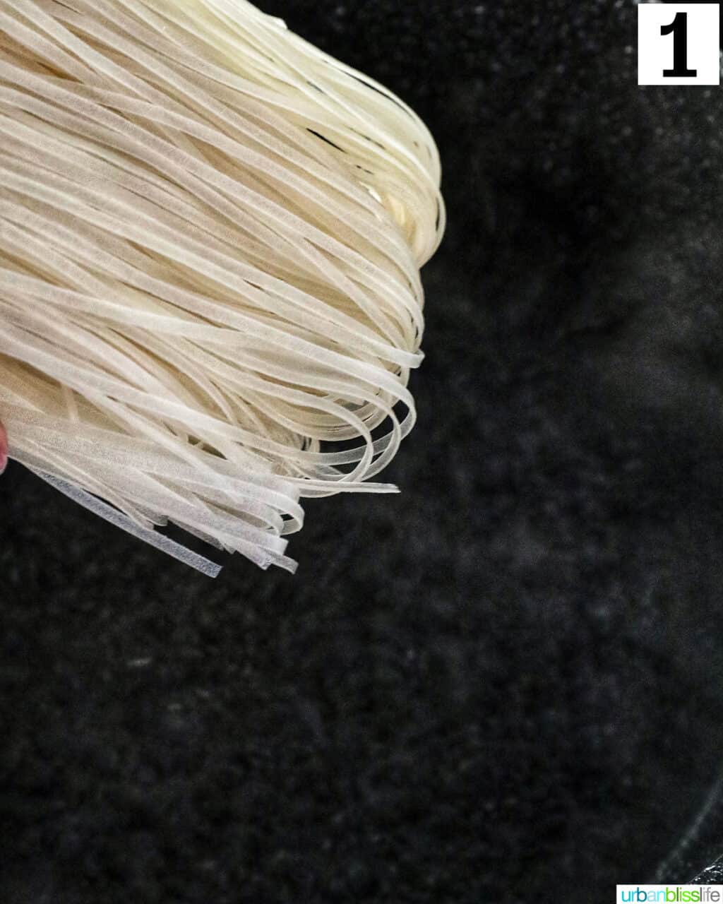 lowering rice noodles into a large pot with water.