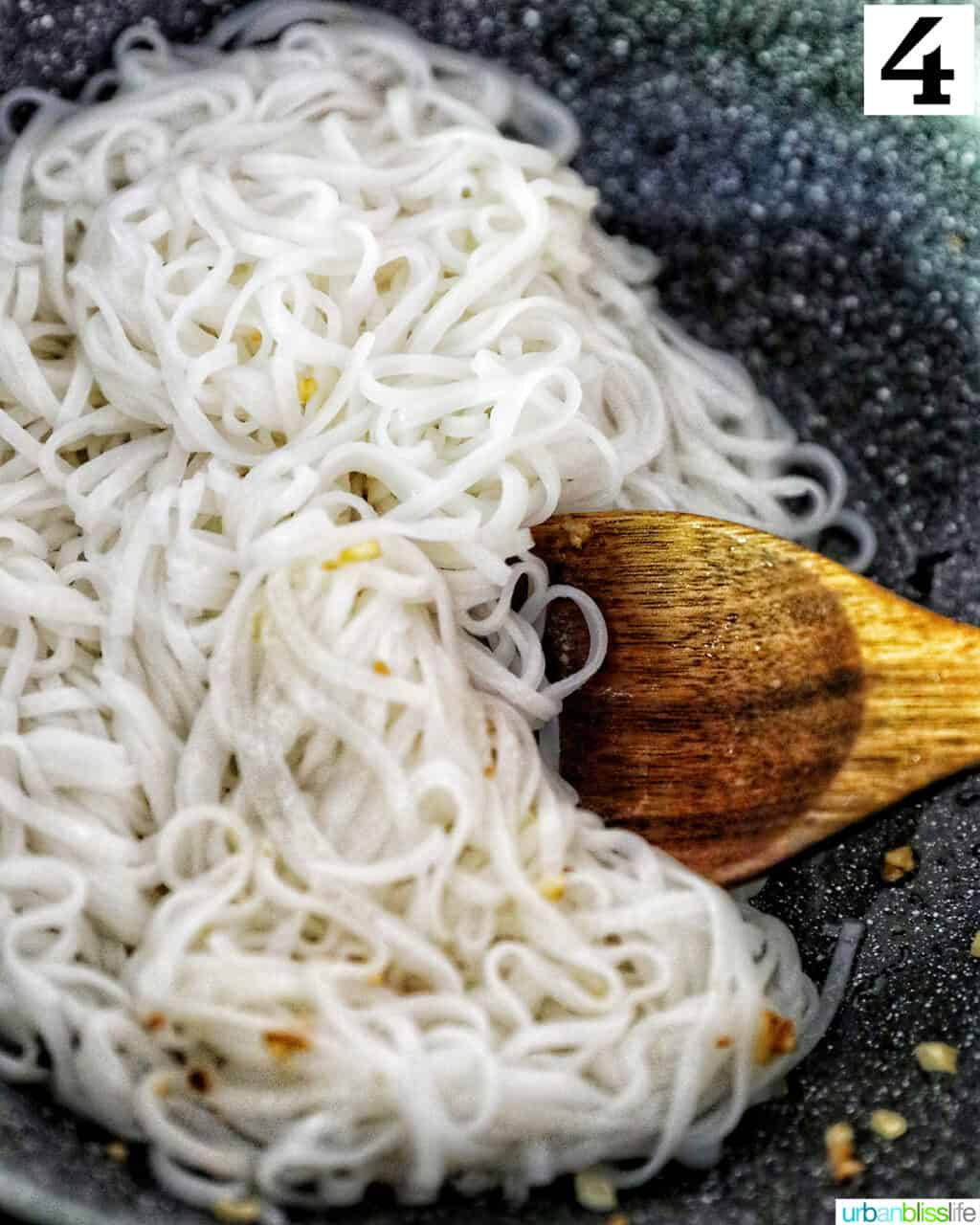 wooden spoon stirring rice noodles in a wok.