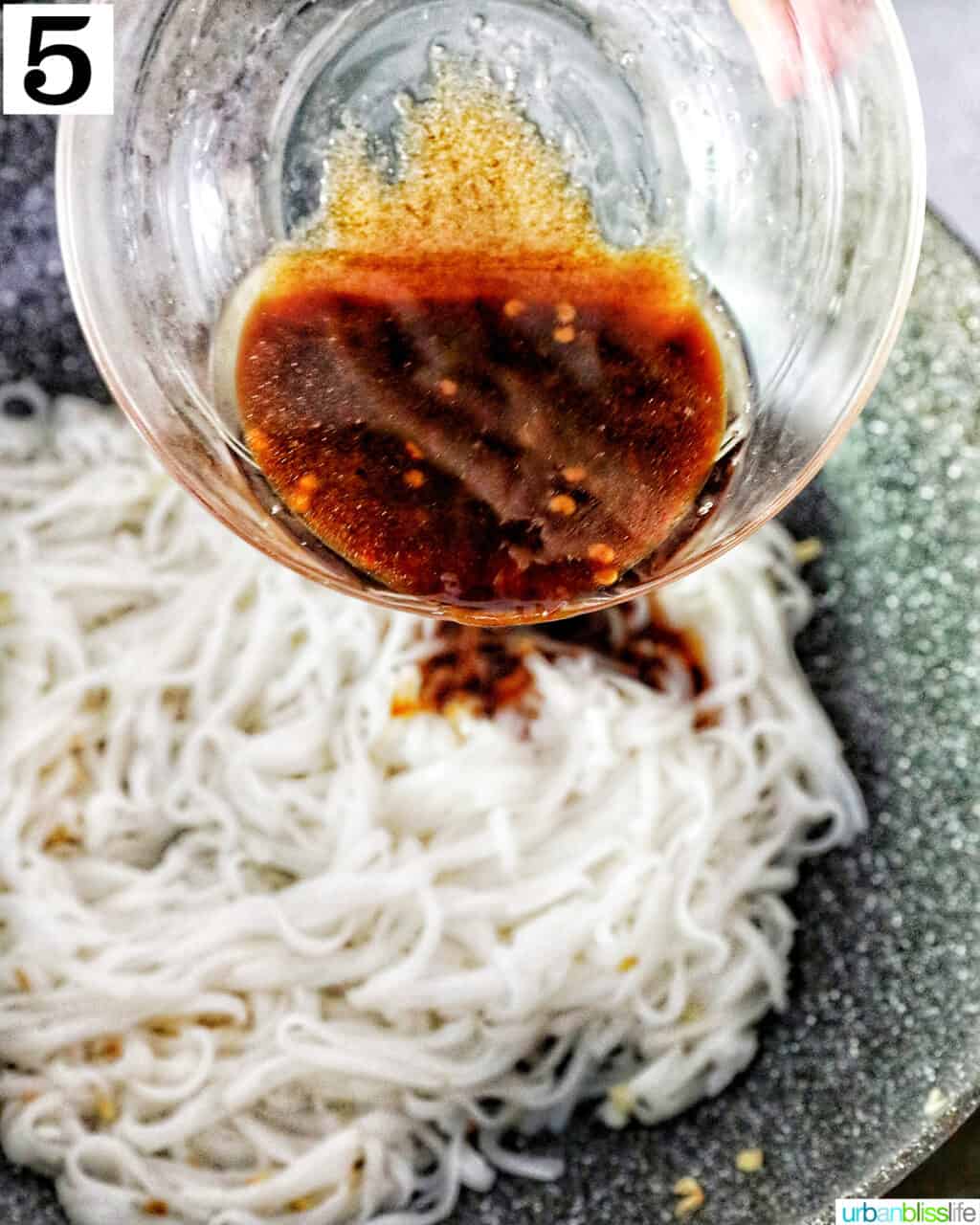 glass bowl of sauce over rice noodles in a wok.