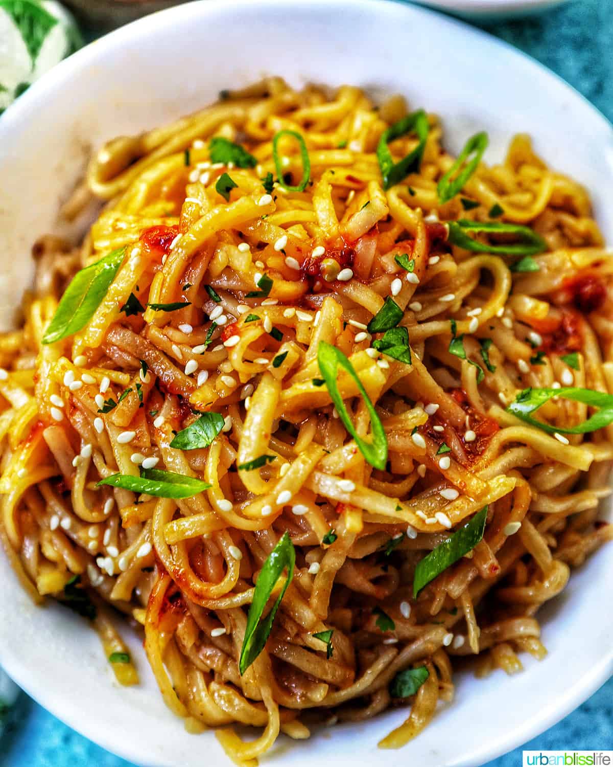 Chili Garlic Noodles with green onions and sesame seeds in a white bowl.