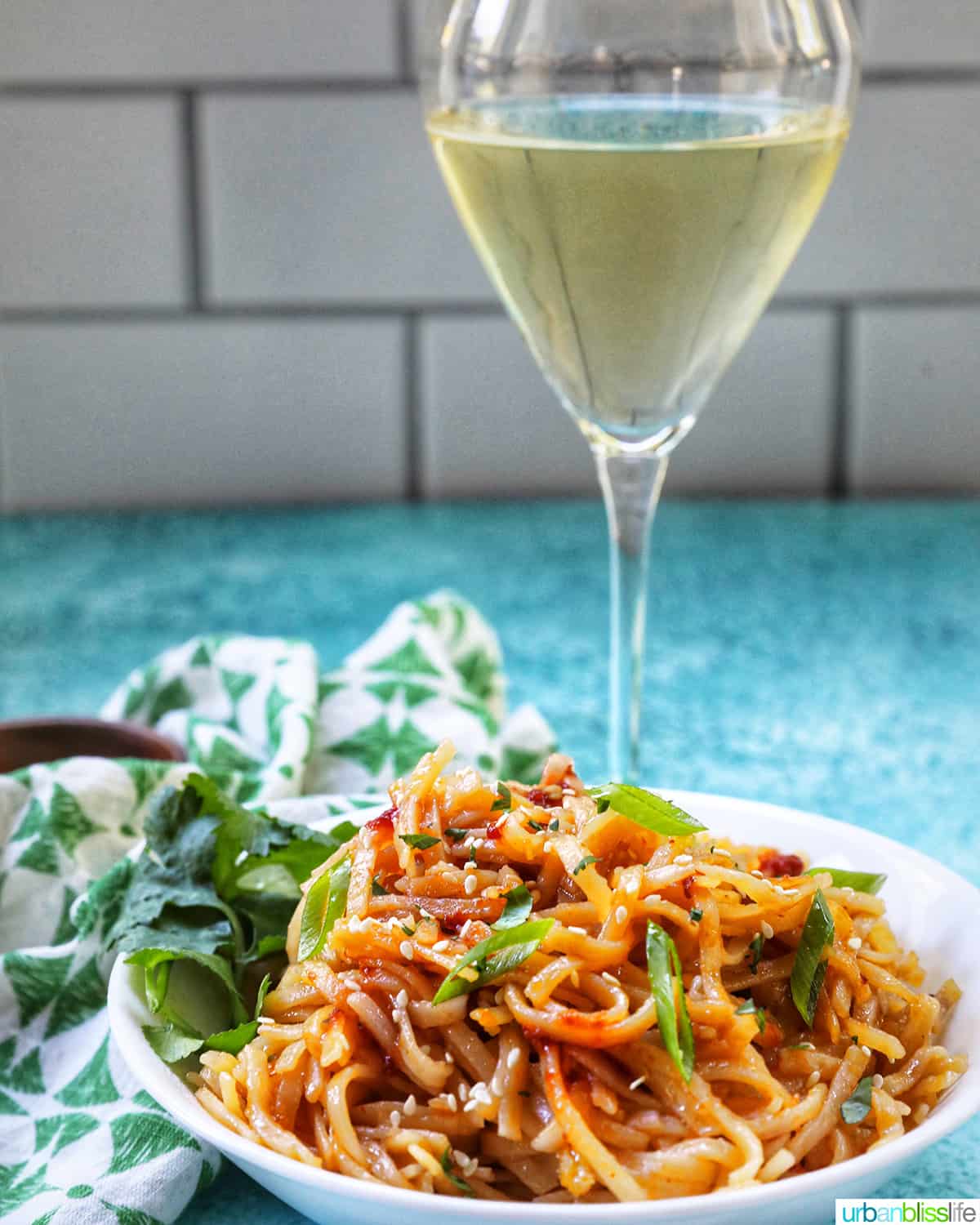 Chili Garlic Noodles with green onions and sesame seeds in a white bowl with a glass of white wine.