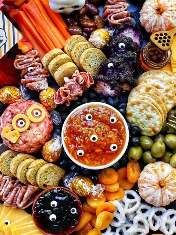 Halloween Charcuterie Board with charcuterie meats, cheeses, crackers, jams, pretzels, fruits, candy eyes, and more orange, purple, and black food.