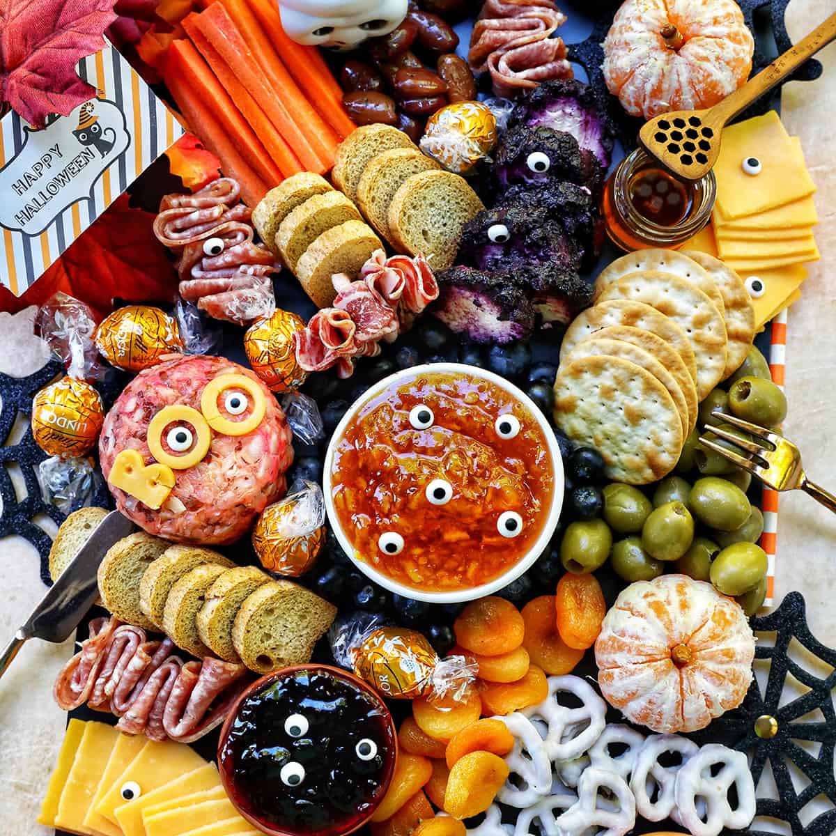 Halloween Charcuterie Board with charcuterie meats, cheeses, crackers, jams, pretzels, fruits, candy eyes, and more orange, purple, and black food.