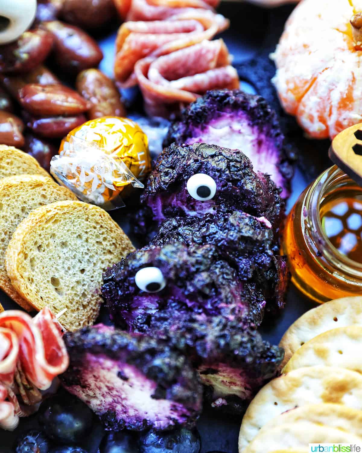 Halloween Charcuterie Board with charcuterie meats, cheeses, crackers, jams, pretzels, fruits, candy eyes, and more orange, purple, and black food.