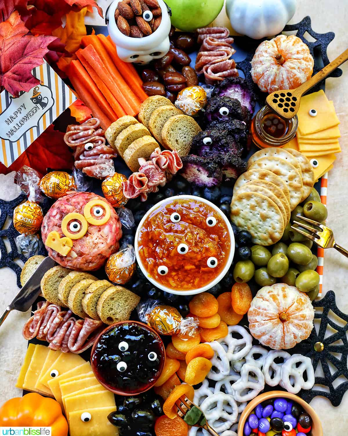 Halloween Charcuterie Board with charcuterie meats, cheeses, crackers, jams, pretzels, fruits, candy eyes, and more orange, purple, and black food.