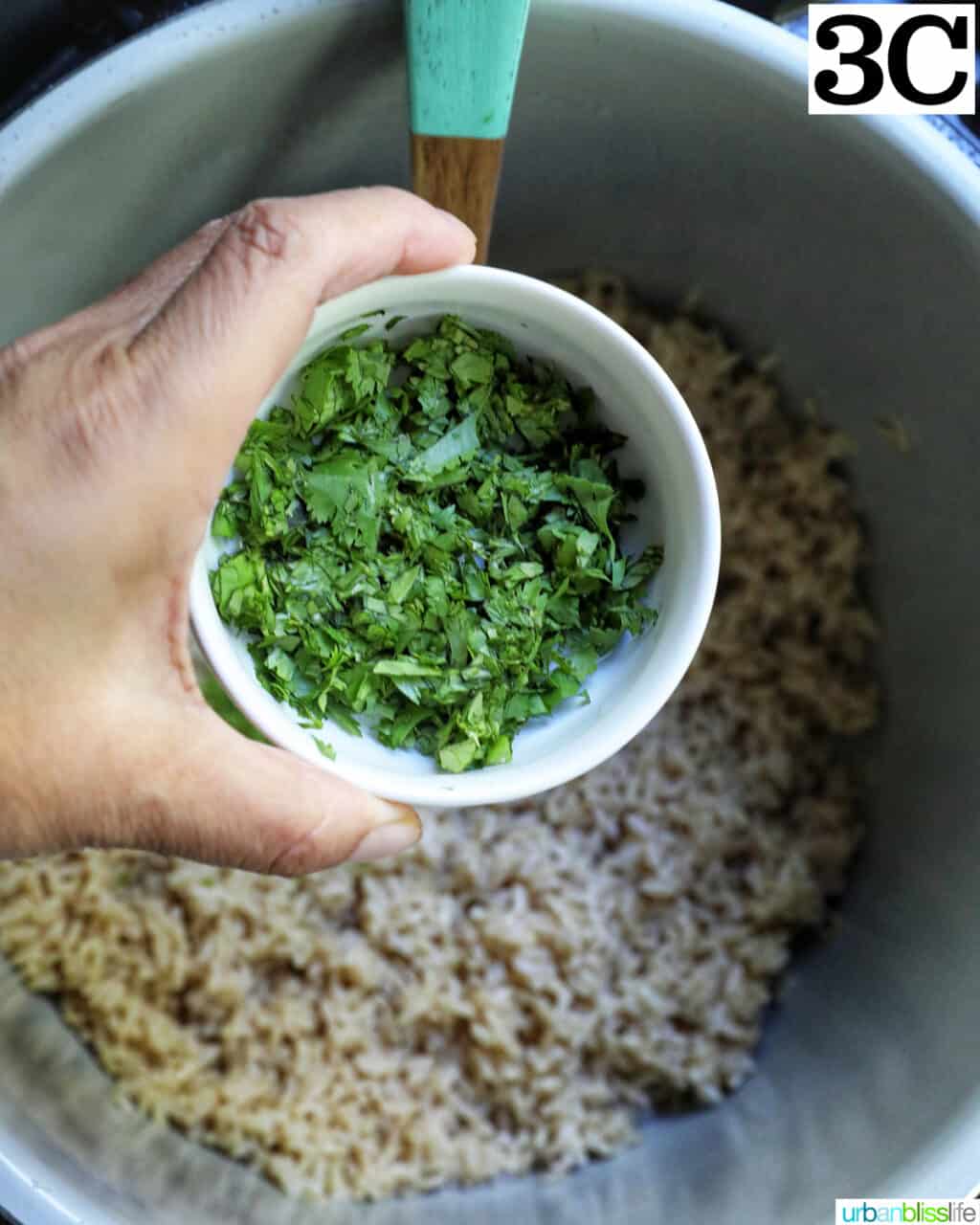 hand holding a bowl of chopped cilantro over brown rice in an instant pot.