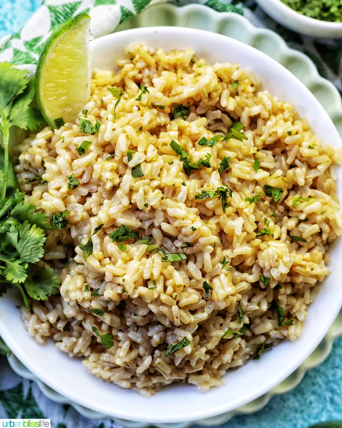 white bowl with Instant Pot Cilantro Lime Brown Rice on a green and white napkin with sides of cilantro leaves and lime wedges.