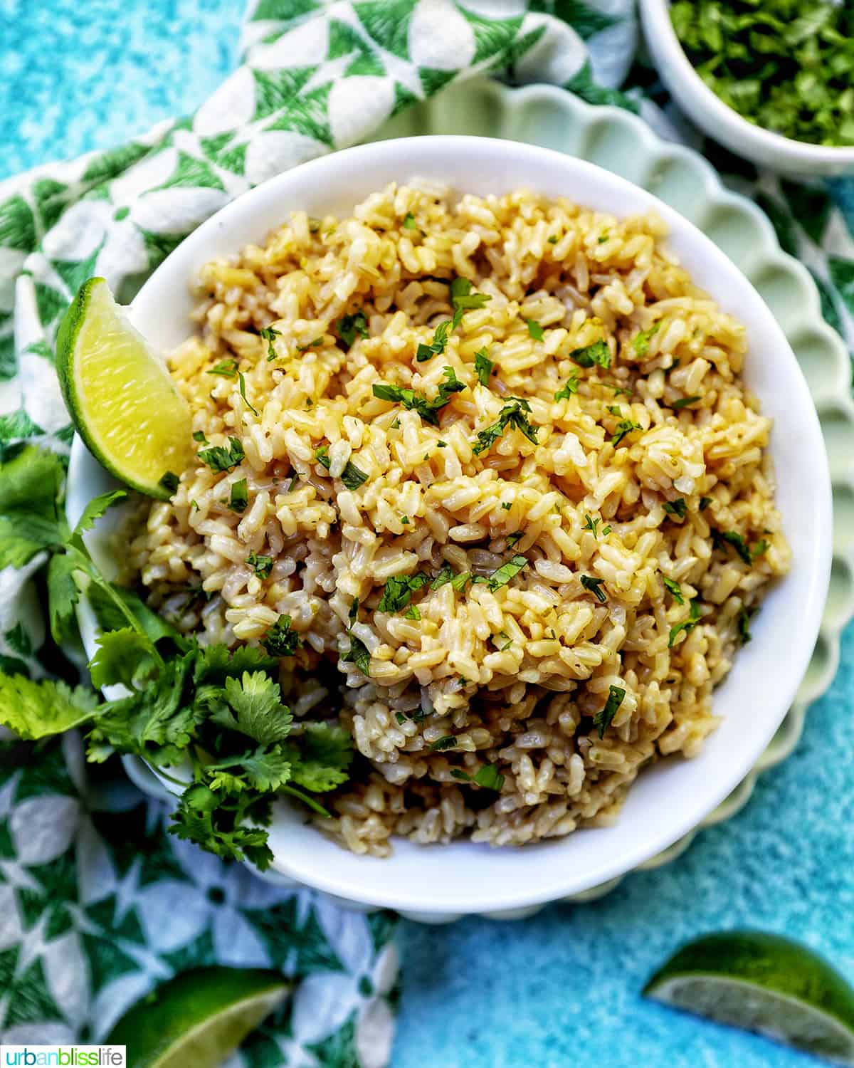 white bowl with Instant Pot Cilantro Lime Brown Rice on a green and white napkin with sides of cilantro leaves and lime wedges.