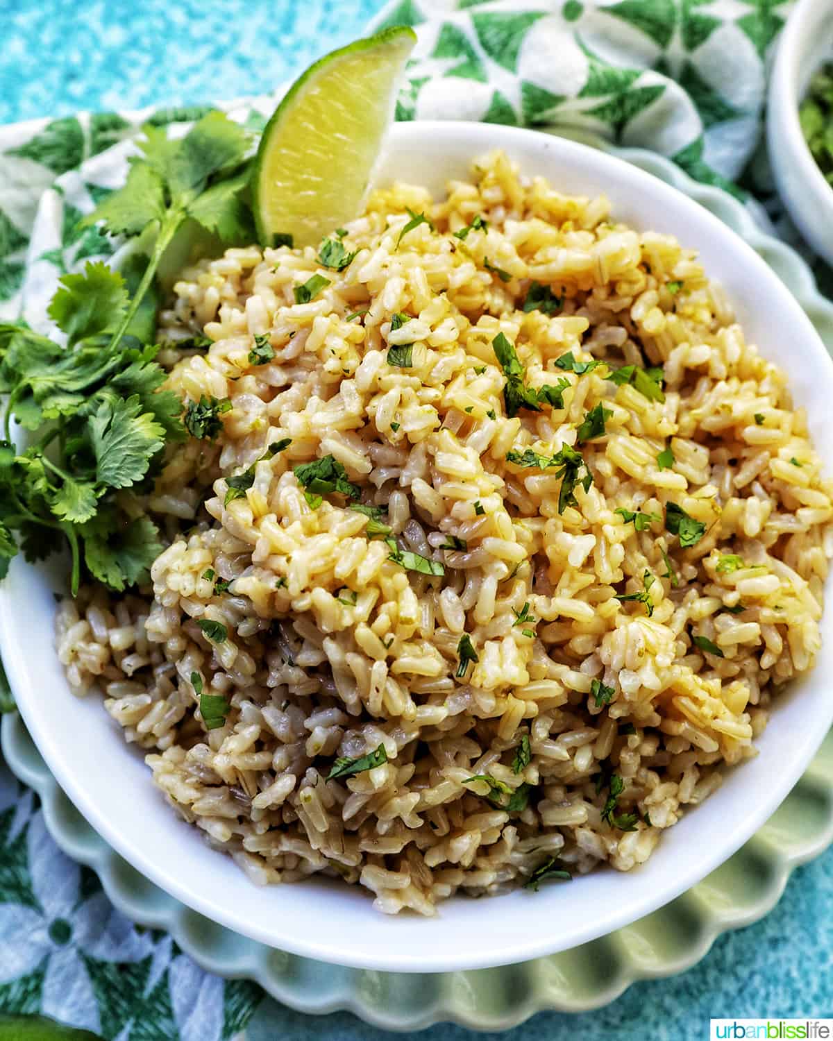 white bowl with Instant Pot Cilantro Lime Brown Rice on a green and white napkin with sides of cilantro leaves and lime wedges.