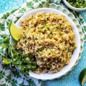 white bowl with Instant Pot Cilantro Lime Brown Rice on a green and white napkin with sides of cilantro leaves and lime wedges.