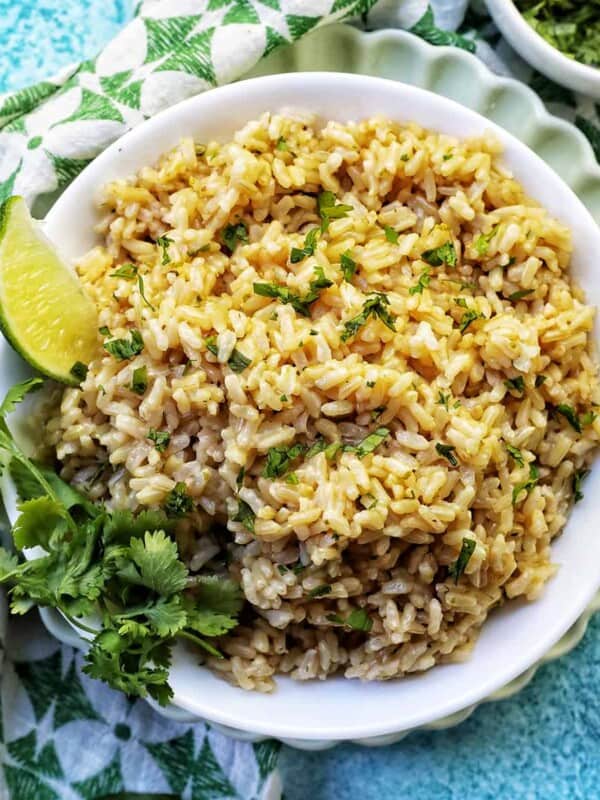 white bowl with Instant Pot Cilantro Lime Brown Rice on a green and white napkin with sides of cilantro leaves and lime wedges.
