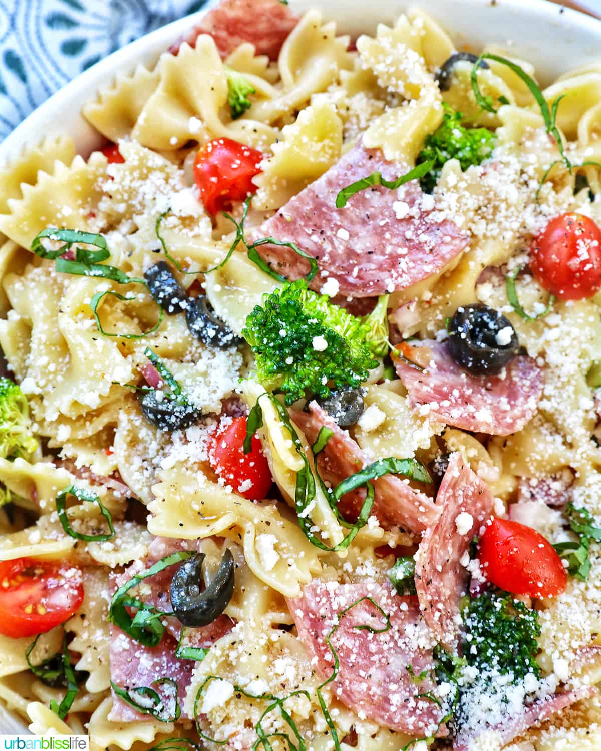 Italian bowtie pasta salad with salami, olives, tomatoes, broccoli, and parmesan cheese in a white bowl.