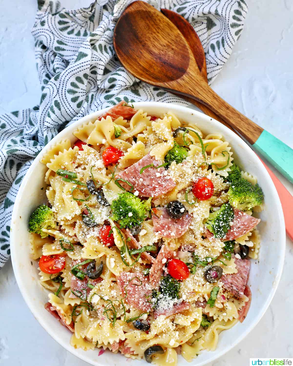 Italian bowtie pasta salad with salami, olives, tomatoes, broccoli, and parmesan cheese in a white bowl.