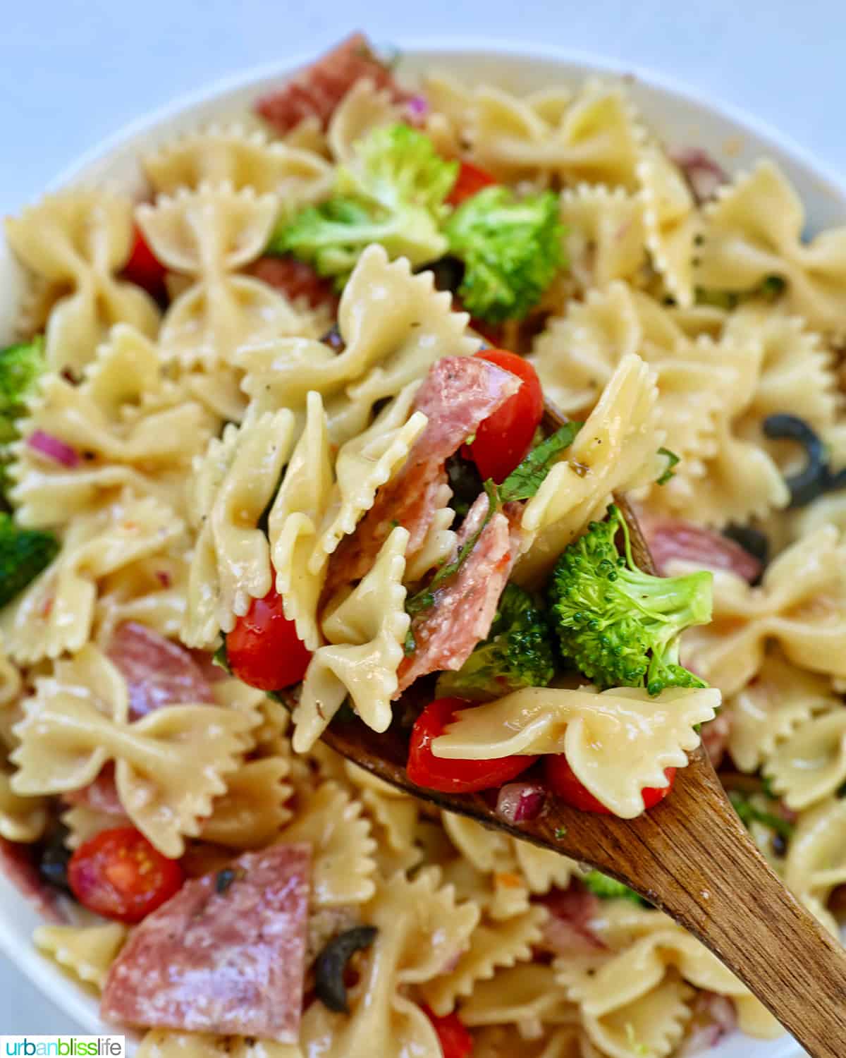 Italian bowtie pasta salad with salami, olives, tomatoes, broccoli, and parmesan cheese in a white bowl.