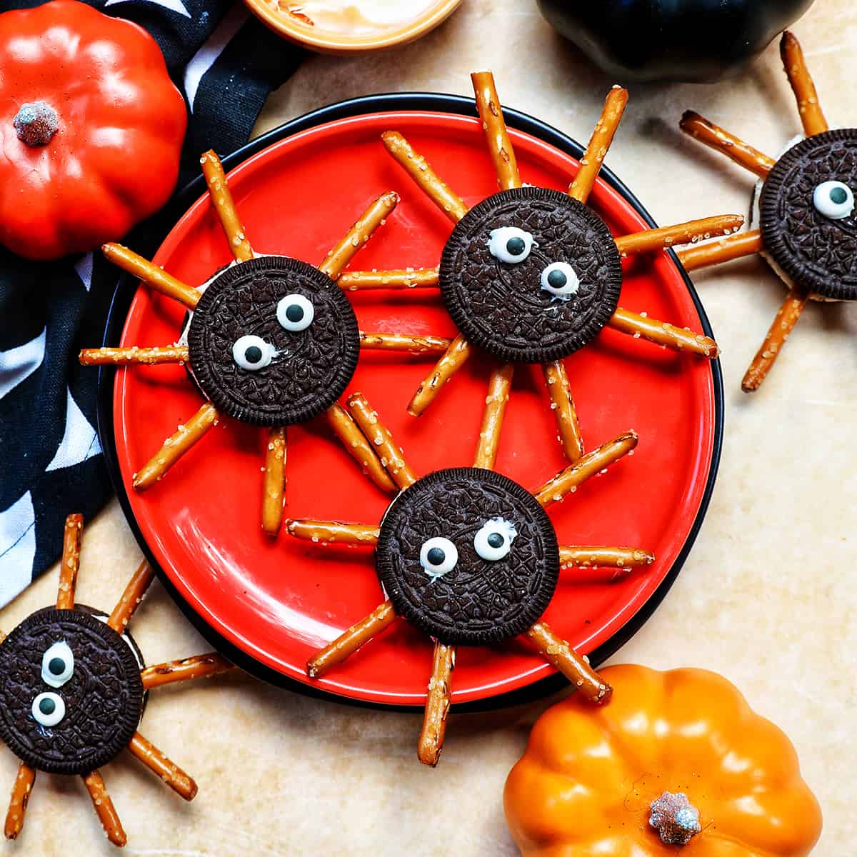 several Oreo Spider Cookies on an orange plate with Halloween decorations around it.