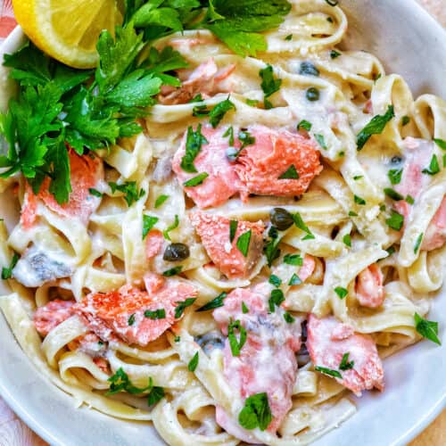 pasta alla salmone with garnishes of parsley and lemon slices in a white bowl.