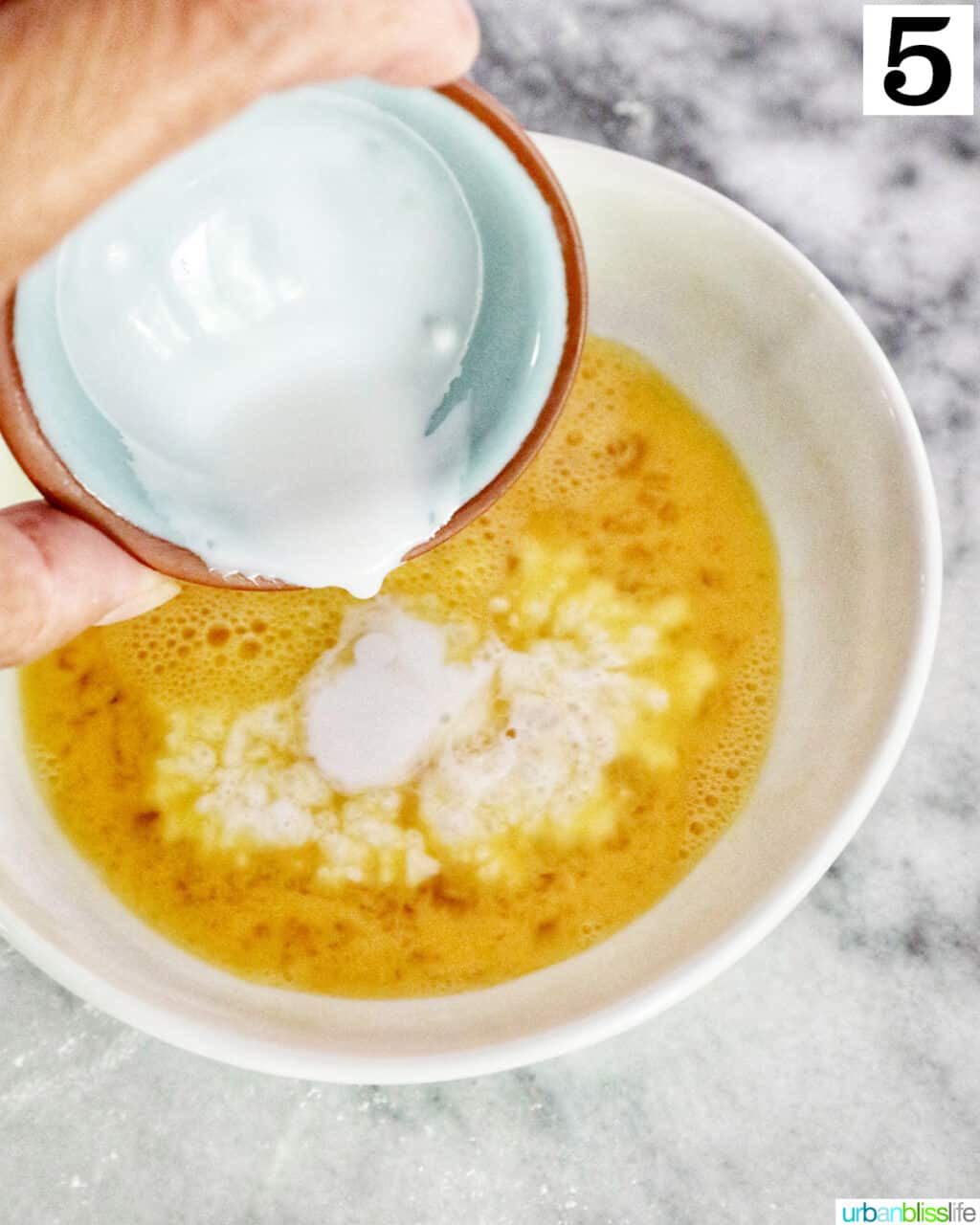 hand pouring cream into a bowl of beaten eggs.