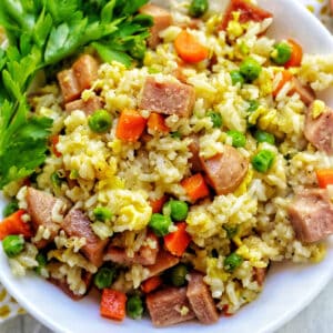 spam fried rice with peas, carrots, and parsley garnish in a white bowl.