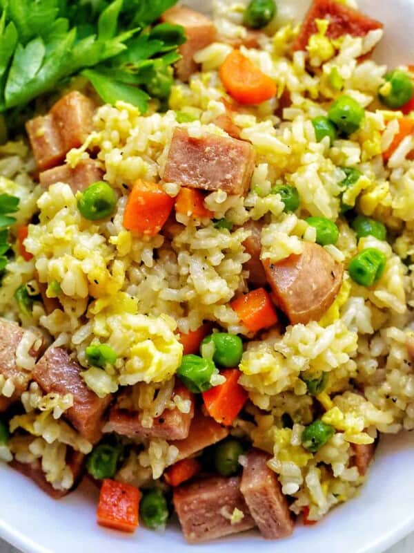 spam fried rice with peas, carrots, and parsley garnish in a white bowl.